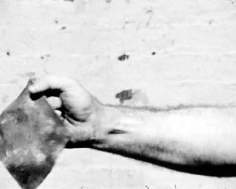 Film still of hand holding a piece of sheet metal