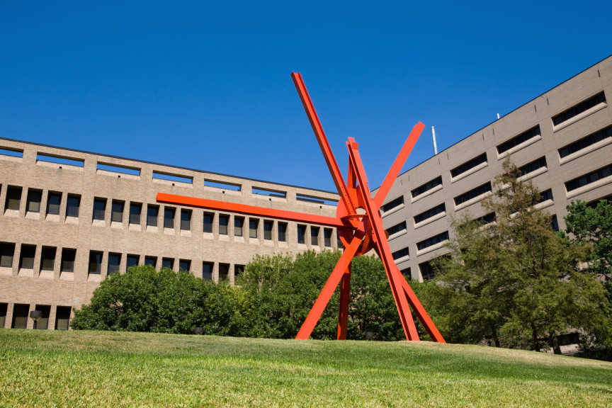 A large sculpture in front of a grey building and blue sky