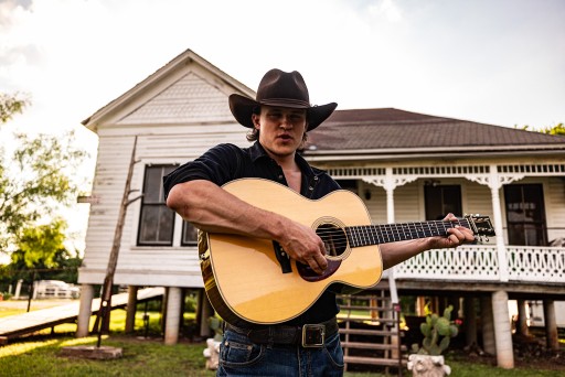 A photograph of musician Coleman Jennings holding a guitar.