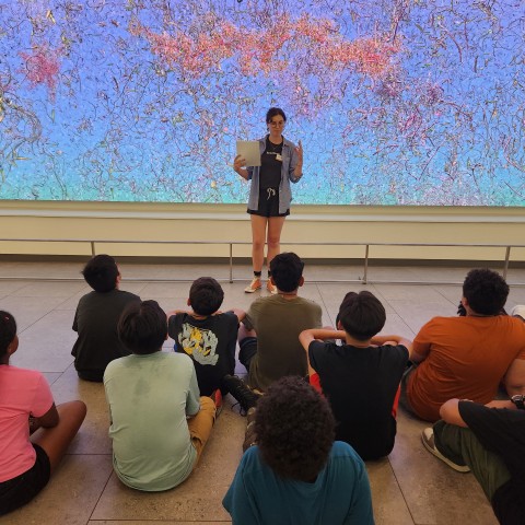 A photo of a person talking to children sitting on the floor in front of Jennifer Steinkamp's "EON"