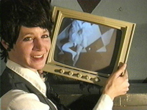 A short haired woman in a vest holding a black and white television