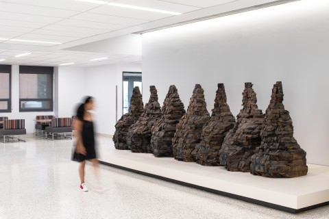 A blurry figure walks in front of Ursula Von Rudingvard's "Untitled (Seven Mountains)"