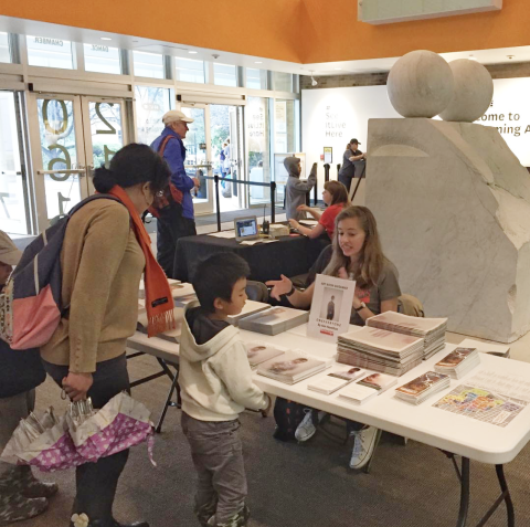 A mother and child looking at a table with Landmarks materials on it with a docent sitting behind the table.