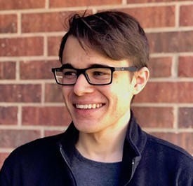 A photo of Thomas Rodriguez; He is smiling and has brown hair and black glasses on and is wearing a navy blue jacket